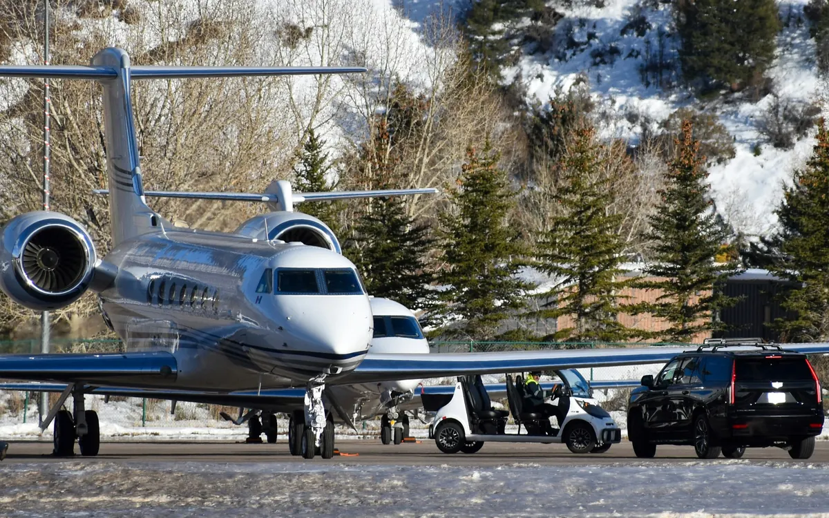 Private jets parked on a snowy ramp among pine trees