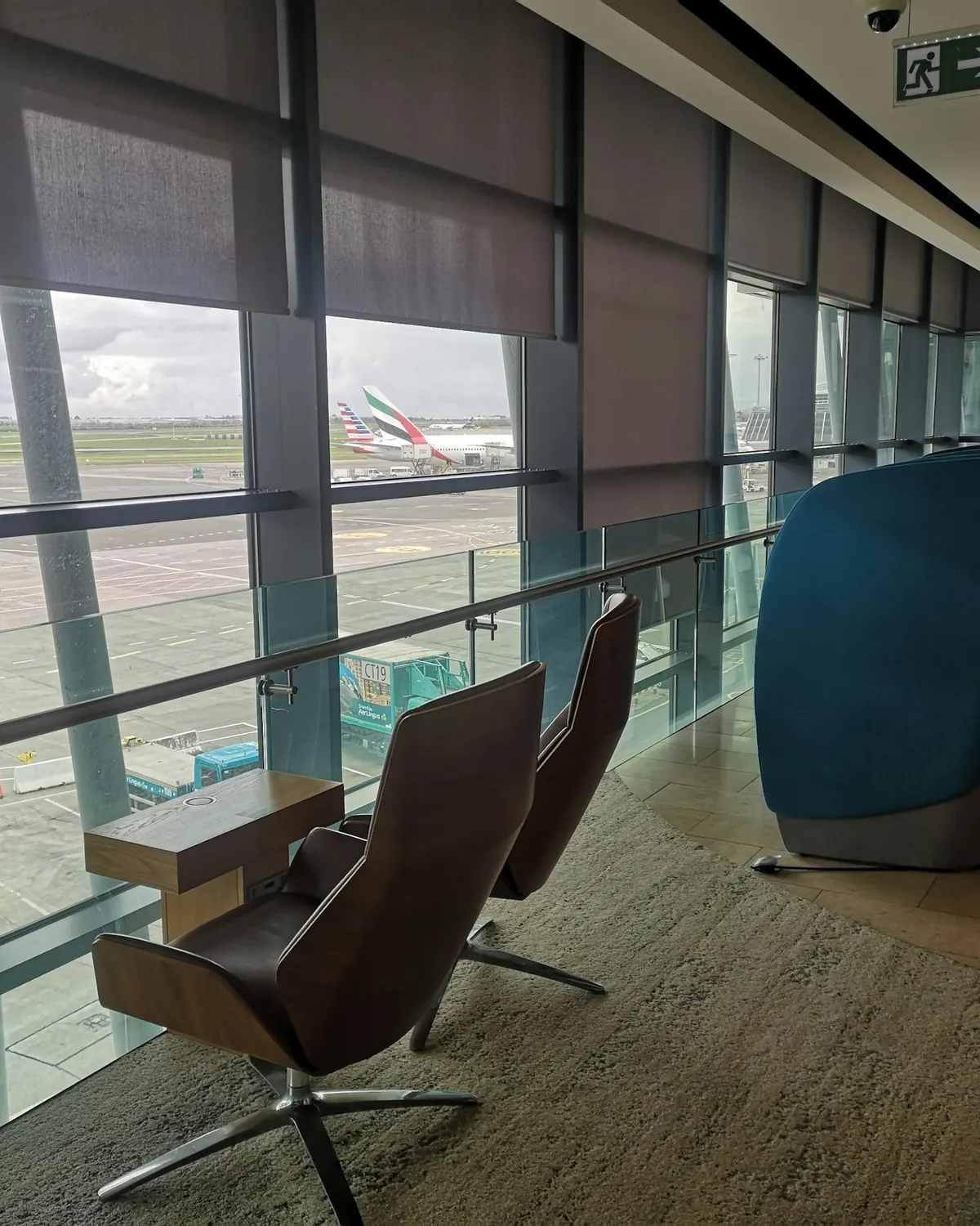 Airport lounge with leather chairs beside tall windows overlooking the apron